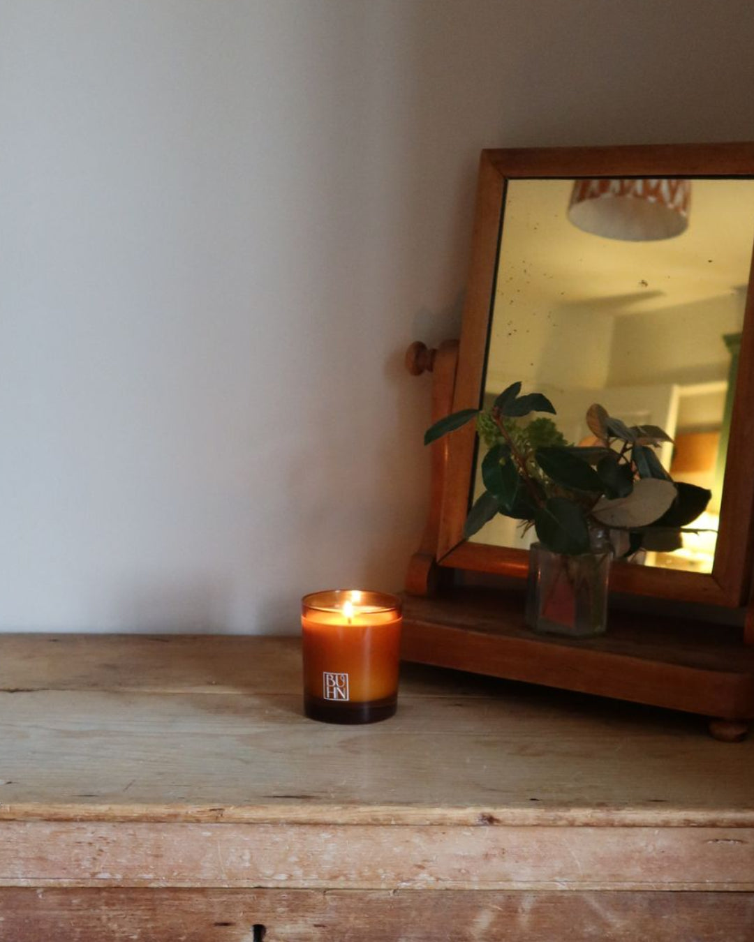 Candle and wooden mirror on a rustic wooden surface with a white wall background